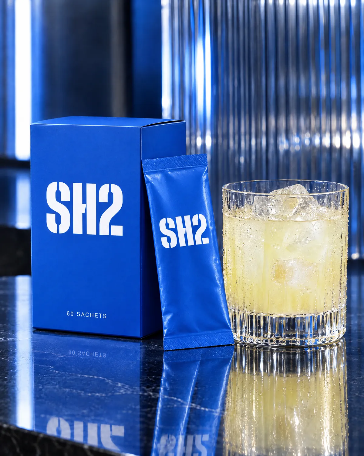 The SH2 box, a sachet and an iced glass on a dark stone bench