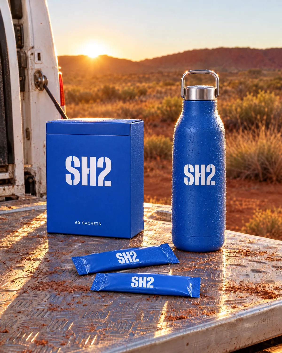 The SH2 box, the steel bottle and two sachets on a ute tray at sunrise in red-dirt country